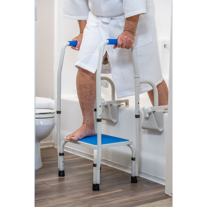 Wearing a white bathrobe, a person uses the Step2Tub Bathtub Step Stool with handles to safely step into the tub in a bathroom with wood floors and a nearby toilet, enhancing safety and fall prevention.