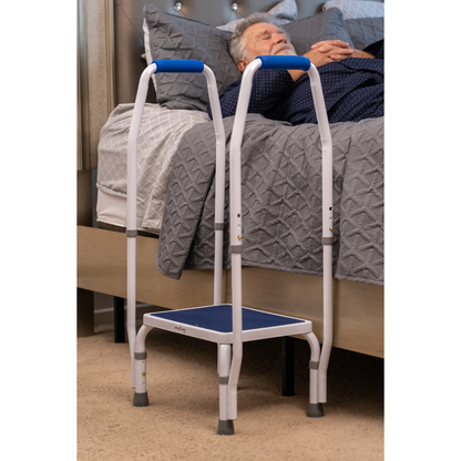 A man lies on a bed with the Step2Bed Mini Bedside Stepper, featuring handrails, positioned beside him to assist with fall prevention and safe bed entry and exit.