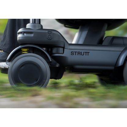 Close-up of a STRUTT Electric Vehicle ev1 mobility scooter wheel in motion outdoors, the brand name clearly visible on the side. Blurred grassy ground emphasizes movement. The STRUTT Electric Vehicle ev1 | Drive Smarter with Guided Sensors meets standard specifications and is not classified as a medical device.