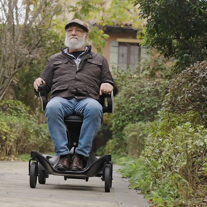 An older man with a white beard, in a cap and jacket, rides his Superpi P2 Portable Electric Wheelchair along an outdoor path lined with greenery and trees, enjoying the accessibility and freedom it offers.