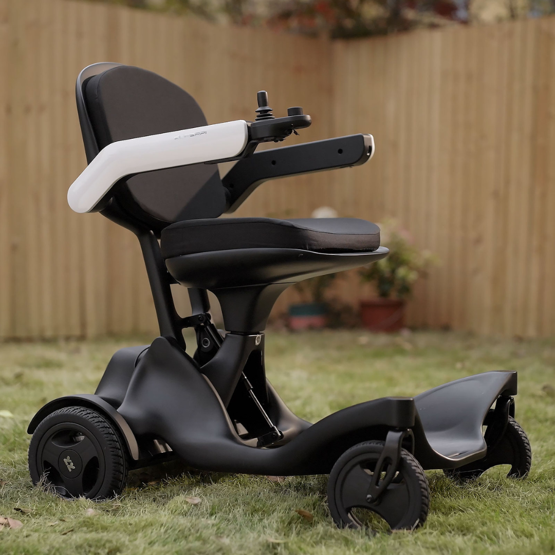 The Superpi P2 Portable Electric Wheelchair, featuring a sleek black and white design, rests on lush backyard grass near a wooden fence and colorful potted plants, creating an inviting outdoor setting.