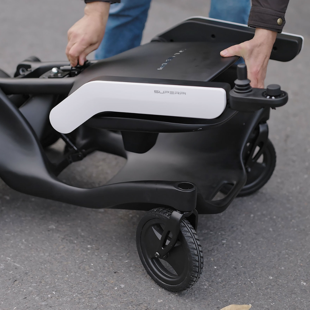 A person folds the Superpi P2 Portable Electric Wheelchair on a paved outdoor surface, preparing it for transport or storage, making it ideal for convenient travel and efficient storage in various settings.