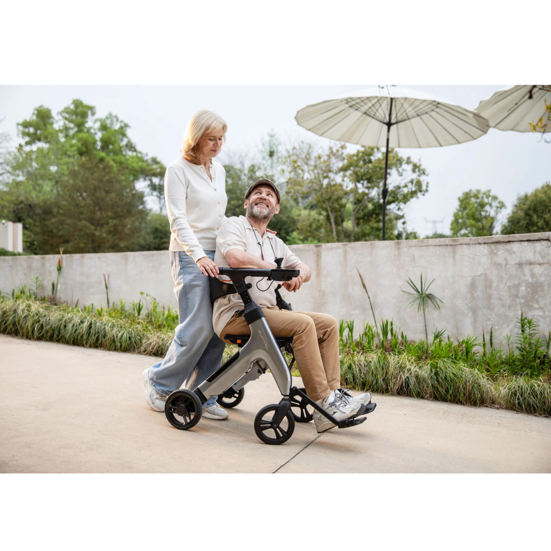 A smiling woman pushes a happy man seated on a Superpi W1 Electric Wheelchair Rollator with 4-in-1 Functionality along an outdoor path, surrounded by greenery and large umbrellas.