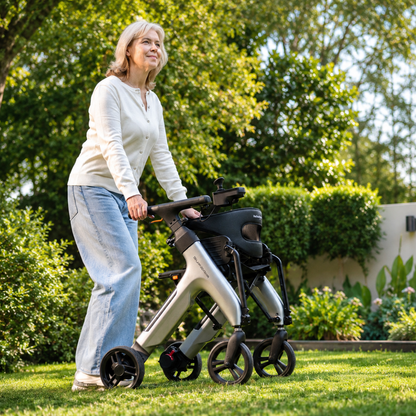 A smiling older woman with gray hair, in a white shirt and blue jeans, enjoys her mobility on a green lawn using the Superpi W1 Electric Wheelchair Rollator with 4-in-1 Functionality surrounded by trees and bushes.