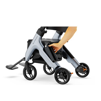 A hand is removing or inserting a battery from the side of the Superpi W1 Electric Wheelchair Rollator, a modern, compact 4-wheel chair with 4-in-1 functionality and a sleek silver frame.