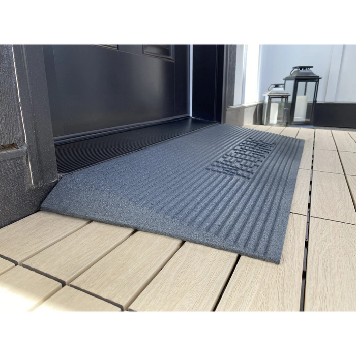 The EZ-Access TRANSITIONS® Angled Entry Welcome Mat is placed at the doorway entrance on a wooden deck for seamless transition, while two decorative lanterns stand in the background next to the door.