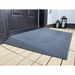 The EZ-Access TRANSITIONS® Angled Entry Welcome Mat, in black with textured grooves and WELCOME, is placed at a dark-colored door entrance for a seamless transition. Nearby, two lanterns on the tiled floor enhance both safety and style.