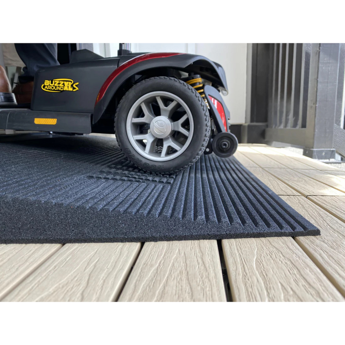 The EZ-Access TRANSITIONS® Angled Entry Welcome Mat, with its textured, slip-resistant rubber surface on a wooden deck, provides stability and traction for smooth transitions of mobility scooters.