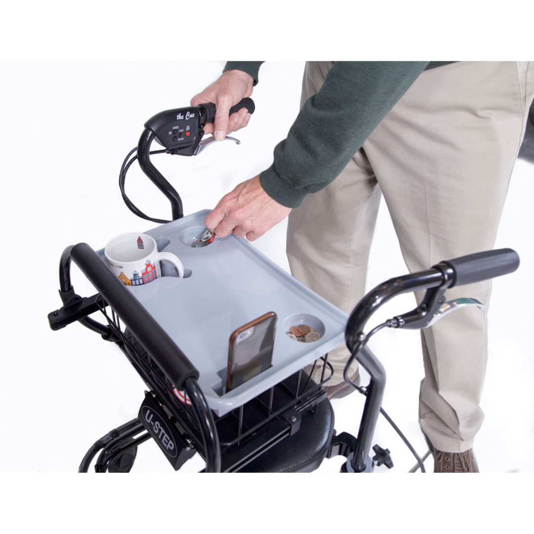 A person uses the In-Step Home Caddy Kit for the U-Step Walker, carrying a mug, phone, and small items, and easily reaches for coins—showing how convenient this caddy is for holding essentials while using a walker.