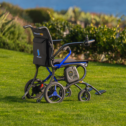 The Forcemech Ultralite G20 PRO Carbon-Fiber Power Wheelchair, featuring a black seat and an eye-catching blue frame, rests on green grass with trees and water softly blurred in the background. Its carbon-fiber construction is complemented by a visible control panel and joystick located on the armrest.
