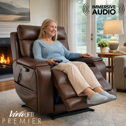 A smiling older woman relaxes with her feet up in the Pride VivaLift! Premier Recliner With Assisted Lift, Audio & Massage. She holds a remote in a bright room with large windows. Text reads: IMMERSE IN AUDIO.