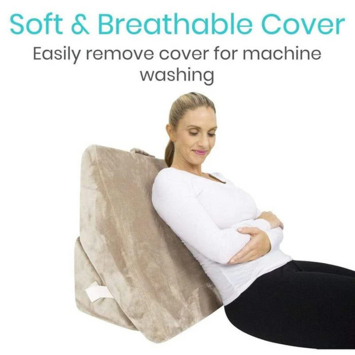 A woman relaxes against a Vive Health Foam Bed Wedge with memory foam, featuring a soft and breathable cover that is easily removable for machine washing. She wears a white top and black pants, enjoying the support of the adjustable incline.