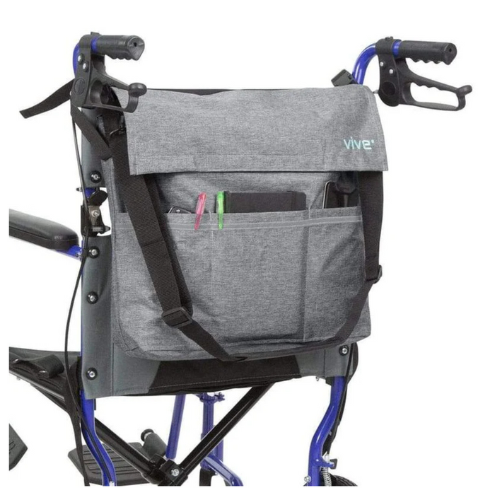 A Vive Health Portable Mobility Bag with Shoulder Strap, made of waterproof nylon in gray, hangs on a blue wheelchairs back. It features adjustable straps and multiple compartments. Pens and a small tablet peek from the front pocket, while the wheelchair’s handles are visible at the top.