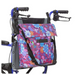 The Vive Health Portable Mobility Bag with Shoulder Strap, crafted from waterproof nylon, attaches to a blue wheelchair. It showcases vibrant floral patterns in blue, pink, and orange. The bag includes adjustable straps for convenience and has two black handles on each side.