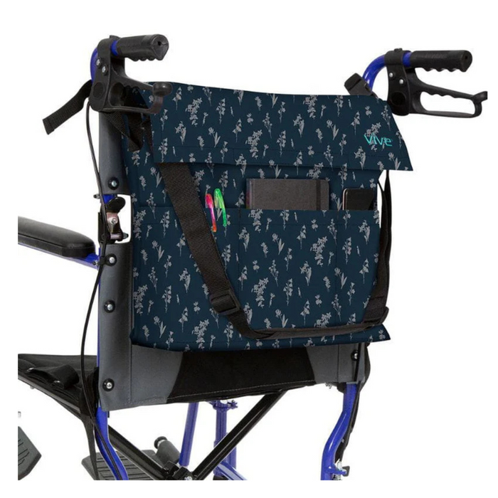 A Vive Health Portable Mobility Bag with shoulder strap hangs on a wheelchairs handles, featuring a dark blue floral design. Made from waterproof nylon, the bag includes multiple compartments for pens and a notebook, adjustable straps, and is designed for convenience and accessibility.