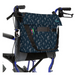 A Vive Health Portable Mobility Bag with shoulder strap hangs on a wheelchairs handles, featuring a dark blue floral design. Made from waterproof nylon, the bag includes multiple compartments for pens and a notebook, adjustable straps, and is designed for convenience and accessibility.