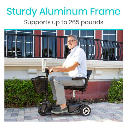 A man smiles while riding the Vive Health 3 Wheel Power Mobility Scooter - Long Range, effortlessly maneuvering along the sidewalk. Its sturdy aluminum frame and comfortable seating support up to 265 pounds as he glides past buildings with large windows and decorative railings.