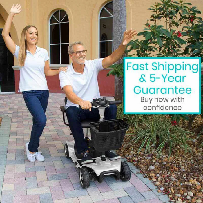 A man rides a Vive Health 4 Wheel Electric Portable Mobility Scooter with comfy swivel seating on a walkway, smiling and waving. A woman waves alongside. Text reads Fast Shipping & 5-Year Guarantee, Buy now with confidence. They are near a beige building with arched windows.