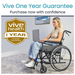 A woman in a Vive Health Air Frame Lightweight Folding Wheelchair uses a laptop. Text above reads Vive One Year Guarantee: Purchase now with confidence, accompanied by a badge that says Vive Health 1 Year Limited Guarantee. A framed landscape picture is on the wall.