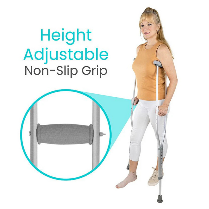 A woman stands using Vive Health Underarm Crutches, wearing a tan top and white pants. The image highlights the crutches height adjustability and non-slip grip, with an inset focusing on the handle, underscoring their role in mobility support.