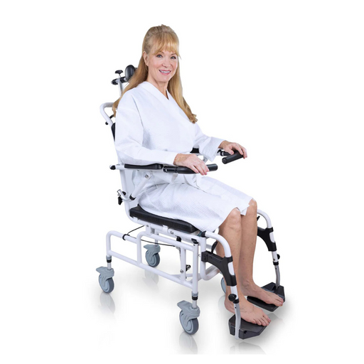 A woman with long hair, wearing a white gown, sits comfortably and smiles on a Vive Health Reclining Shower Commode Transport Chair. This versatile 3-in-1 design features wheels and footrests for mobility support against a plain white background.