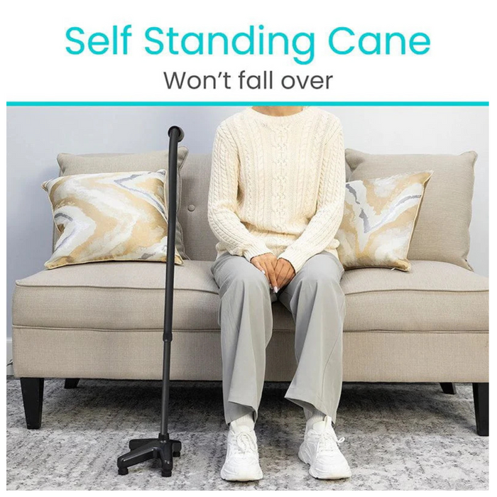 A person in a cream sweater and gray pants sits on a beige couch with patterned cushions. Next to them stands the Vive Health SureWalk Stand-Alone Quad Cane, crafted from heavy-duty aluminum with an ergonomic handle. Text reads, Self Standing Cane Wont Fall Over.