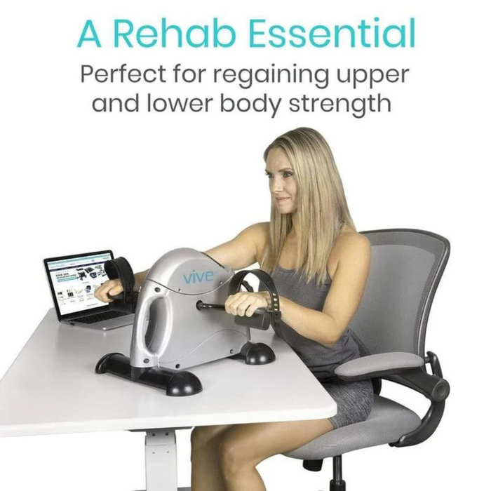 A woman sits in a chair using the Vive Health Portable Pedal Exerciser on a white desk, with an open laptop beside her. Text above reads: A Rehab Essential. With adjustable resistance, its ideal for regaining upper and lower body strength.