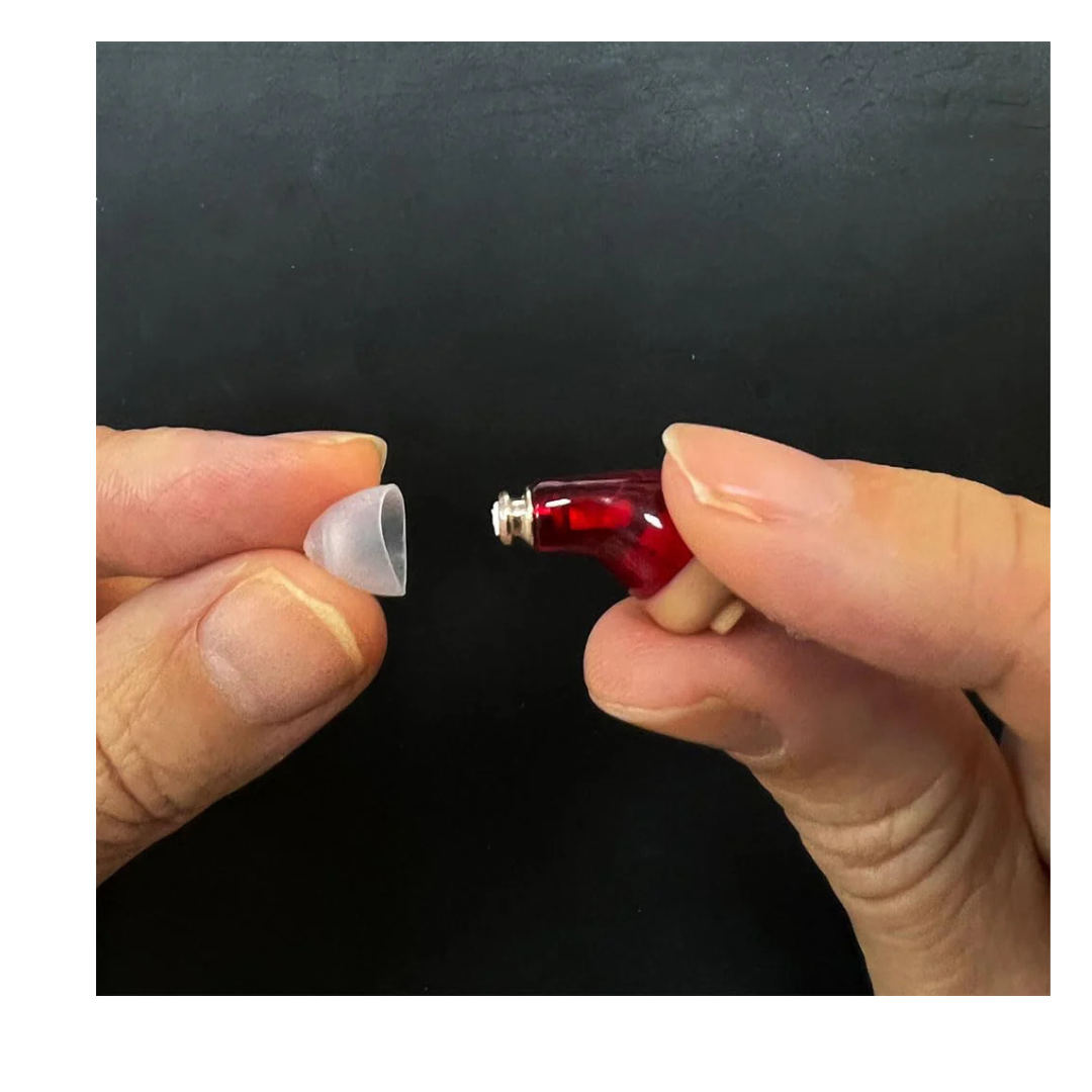 A close-up shows two hands with Vivtone Ear Tip Replacements for Super-Mini Hearing Aids: one holding a red in-ear device, the other holding a small translucent CIC dome, ready to attach the replacement ear tip.