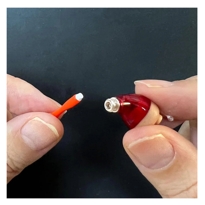 Two hands hold Vivtone Ear Wax Guards for Hearing Aids: one with a red, cone-shaped piece featuring a metal socket, and the other with an orange rod with a white tip. Both are shown against a black background.