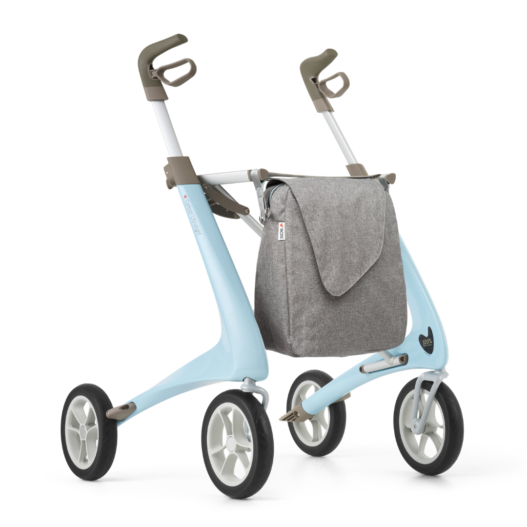 A stylish Weekend Bag for ByAcre Carbon Fiber Rollators features a large grey fabric design, pairing seamlessly with the modern rollator’s light blue frame, ergonomic grey handles, and four black-and-white wheels for practical everyday use.