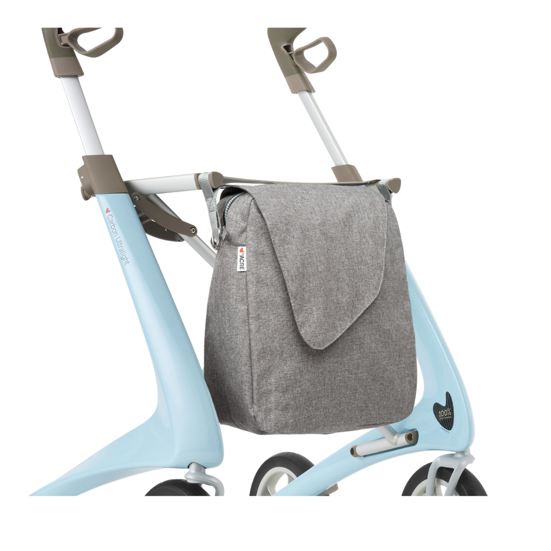 The Weekend Bag for ByAcre Carbon Fiber Rollators is a gray fabric flap bag attached to a light blue four-wheeled walker frame, ideal for carrying specs or essentials, shown against a white background.