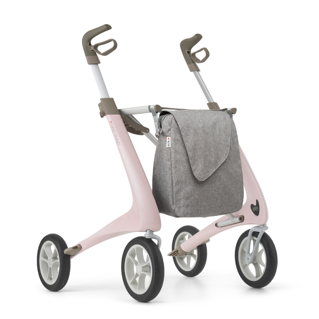 A large gray Weekend Bag, designed for ByAcre Carbon Fiber Rollators, attaches to the walker’s frame. Shown on a white background with a modern pink rollator featuring gray handlebars and a minimalistic, table-inspired look.