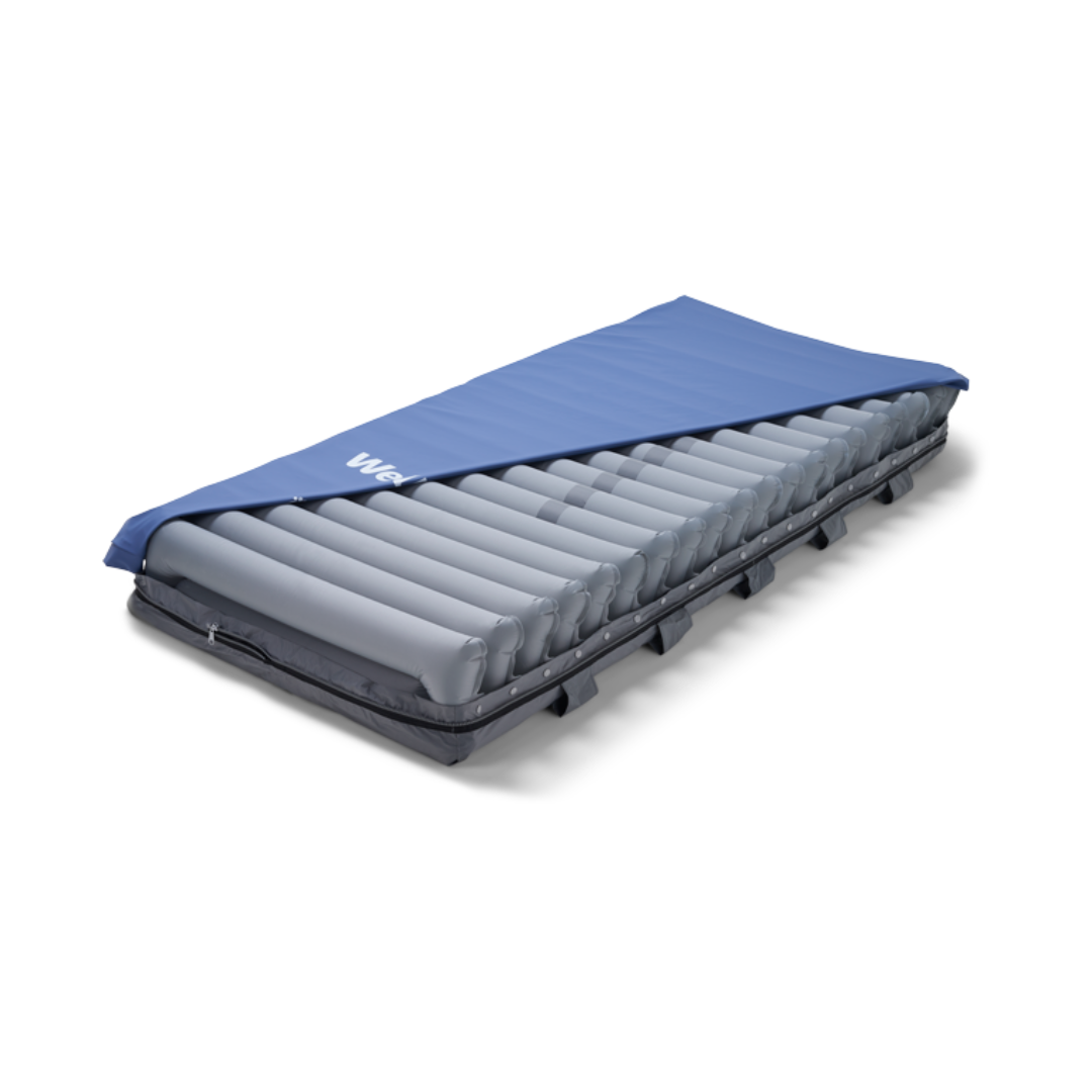 The Wellell Domus Auto G2 Bariatric Alternating Pressure and Low Air Loss System, shown with its blue cover partially pulled back to reveal grey air tubes, is designed for pressure ulcer prevention and sits on a low bed frame.
