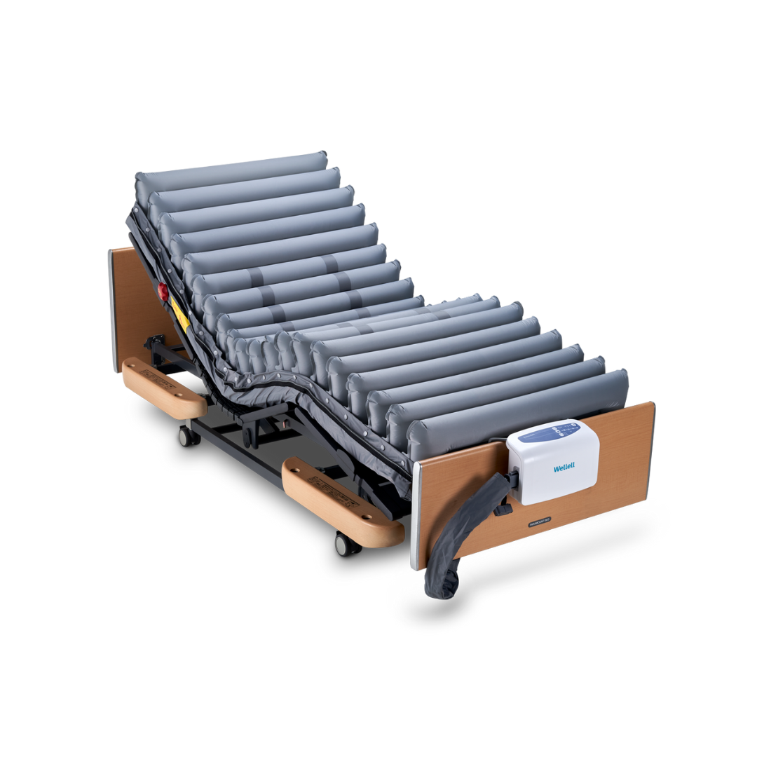 The Wellell Domus Auto G2 Bariatric Alternating Pressure and Low Air Loss System features an adjustable hospital bed with a gray mattress, a white electronic control unit at the foot, wooden head/foot panels, and a sturdy black metal frame.