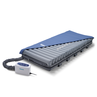 The Wellell Procare Elite Alternating Pressure Mattress with Micro Low Air Loss, partly covered by a blue sheet and connected to a white pump, is designed for effective pressure injury and bedsore prevention.