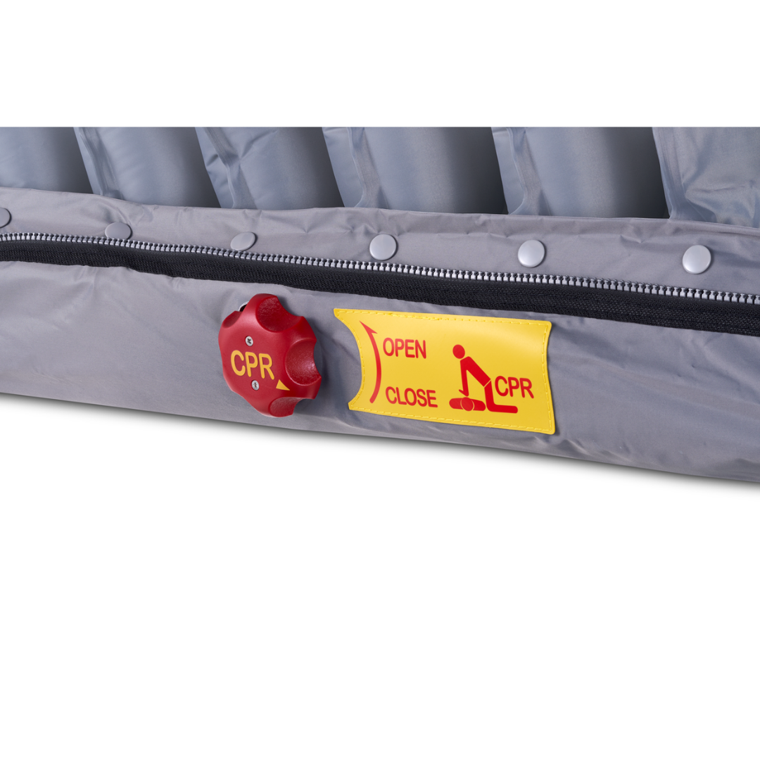 Close-up of the Wellell Serene Air Alternating Pressure Mattress with True Low Air Loss, showing a gray cover, red CPR valve, yellow instruction label, zipper, and visible air chambers for pressure injury prevention.