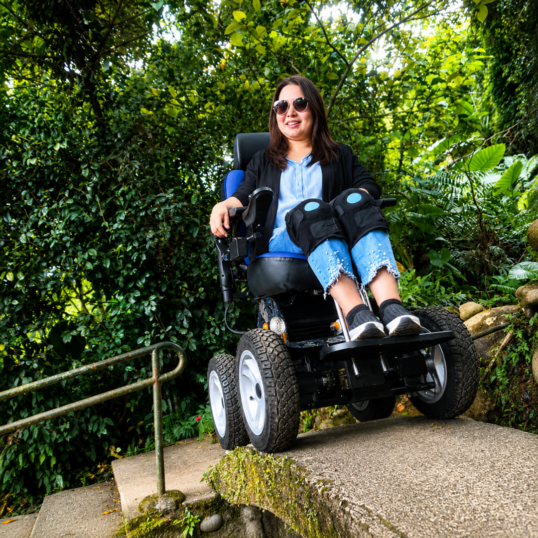 A woman in sunglasses and a blue shirt smiles while using the Wheelchair88 All-Terrain Stair Climbing 4x4 Recreational Electric Vehicle with gyro balance technology along an outdoor path surrounded by lush greenery.