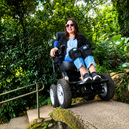 A woman in sunglasses and a blue shirt smiles while using the Wheelchair88 All-Terrain Stair Climbing 4x4 Recreational Electric Vehicle with gyro balance technology along an outdoor path surrounded by lush greenery.