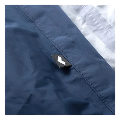 A close-up of the Waterproof Cover For Whill Model C2 Power Chairs in blue, showing a small black tag with a white geometric logo near the seam, and light gray fabric visible along the upper right edge.