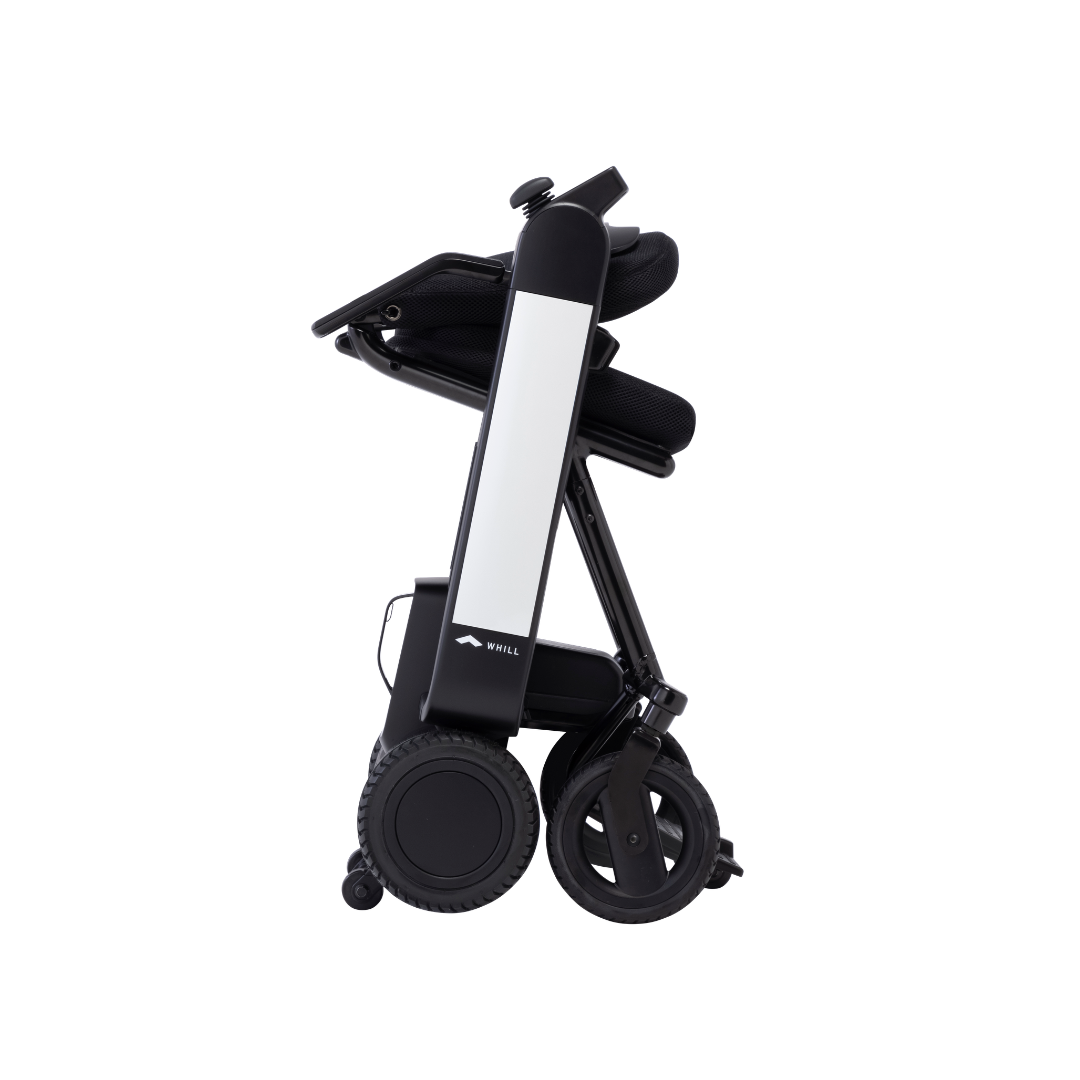 The Whill Model F Lightweight Portable Electric Wheelchair is shown folded upright, featuring four visible wheels and a compact, vertical design for easy storage or transport. Check Specifications, Downloads, or Videos for more details.