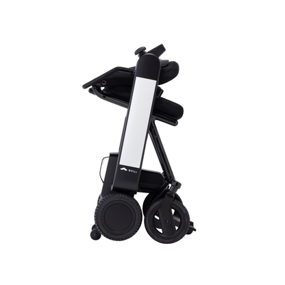 The Whill Model F Lightweight Portable Electric Wheelchair is shown folded upright, featuring four visible wheels and a compact, vertical design for easy storage or transport. Check Specifications, Downloads, or Videos for more details.