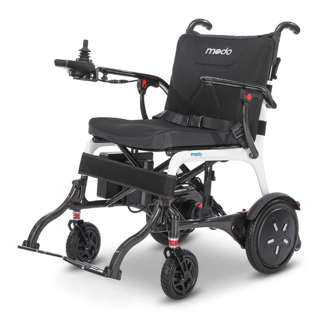Introducing the Whill MODO Breeze Ultra-Lightweight CF Folding Electric Wheelchair: a modern mobility solution featuring a black seat, armrests, footrests, and intuitive joystick controls. Its white frame complements the compact design with four wheels for stability, while its foldable construction allows for easy storage and transport.