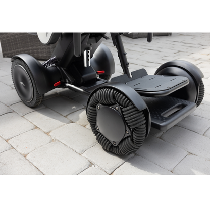 Close-up of the wheels and footrest of the Whill Model C2 Smart Power Chair - Compact Portable Mobility, a modern mobility device, on a light gray stone patio. The wheels feature a distinctive spiral tread pattern.
