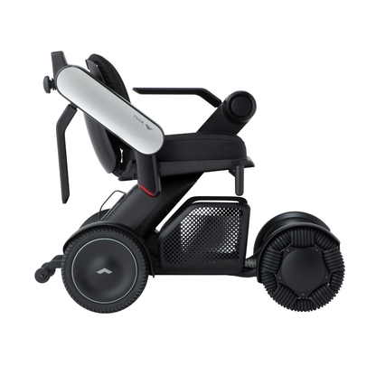The Whill Model C2 Smart Power Chair is a compact, portable mobility device in sleek black and white, featuring large rear wheels, mesh side panel, ergonomic armrests, and FDA-compliant Class II safety. Shown in profile on a white background.