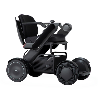 The Whill Model C2 Smart Power Chair - Compact Portable Mobility is a modern electric wheelchair with large wheels, black frame, armrests, and a mesh basket under the seat, designed for enhanced accessibility and mobility as a Class II medical device.