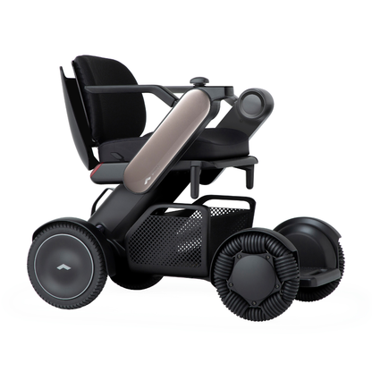 The Whill Model C2 Smart Power Chair - Compact Portable Mobility features a sleek black and metallic design, large wheels, padded seat, mesh storage basket, and futuristic armrests. It’s a Class II medical device with modern, minimalist style.