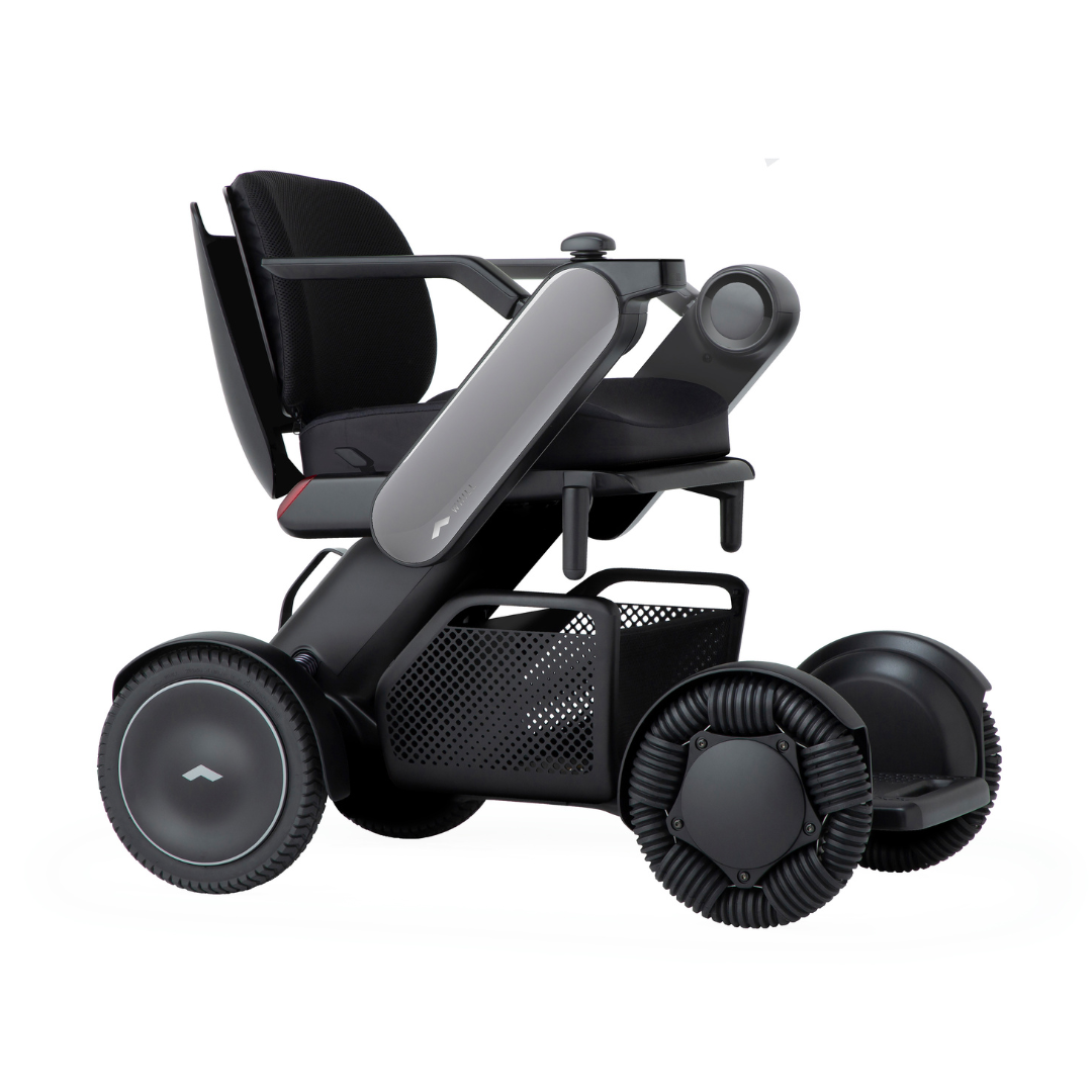 The Whill Model C2 Smart Power Chair is a compact, portable mobility device in black with large wheels, a mesh basket under the seat, contoured armrests, and minimalistic design—engineered as an FDA-compliant Class II medical device.