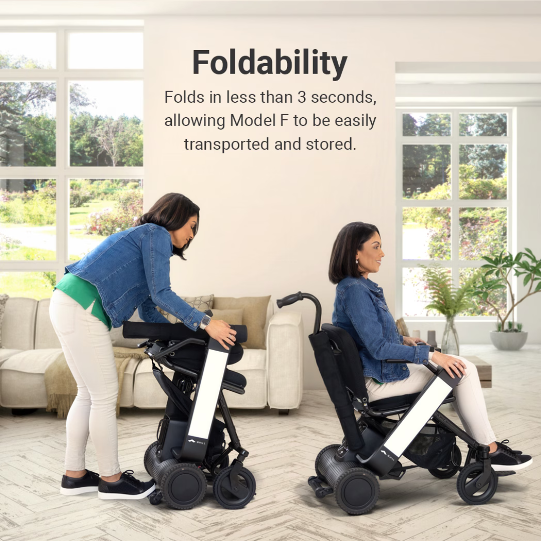 Two women in a living room show how the Whill Model F Lightweight Portable Electric Wheelchair folds in under 3 seconds for easy transport and storage, as one sits and another folds an identical chair. See above for specifications and warranty.