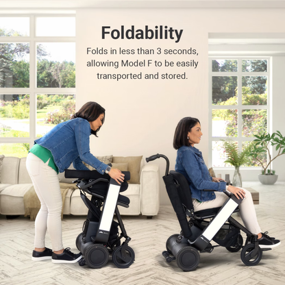 Two women in a living room show how the Whill Model F Lightweight Portable Electric Wheelchair folds in under 3 seconds for easy transport and storage, as one sits and another folds an identical chair. See above for specifications and warranty.