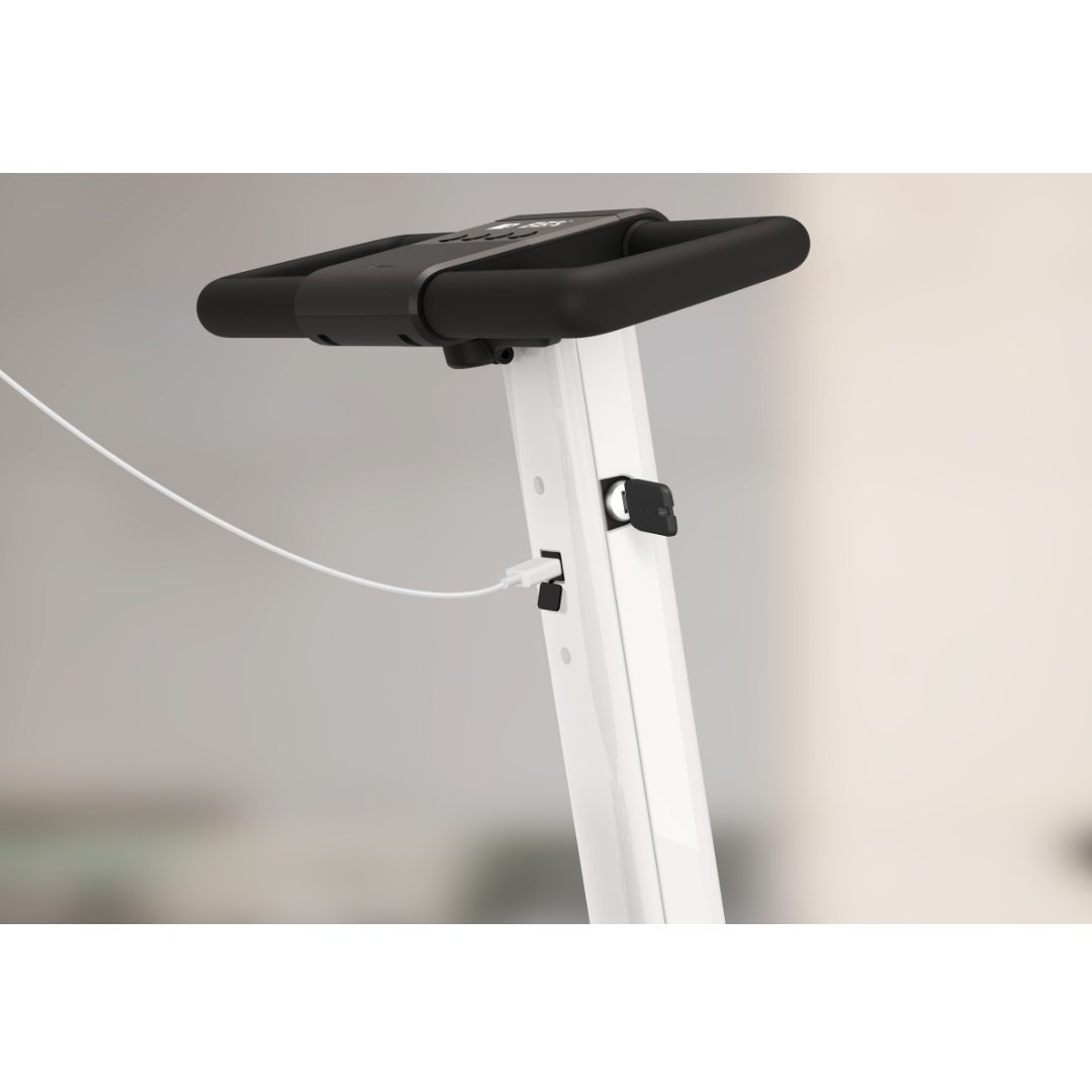 Close-up of a Whill Model R 3-Wheel Mobility Scooter frame with a small digital display and a charging cable connected to the USB port. Background is blurred.